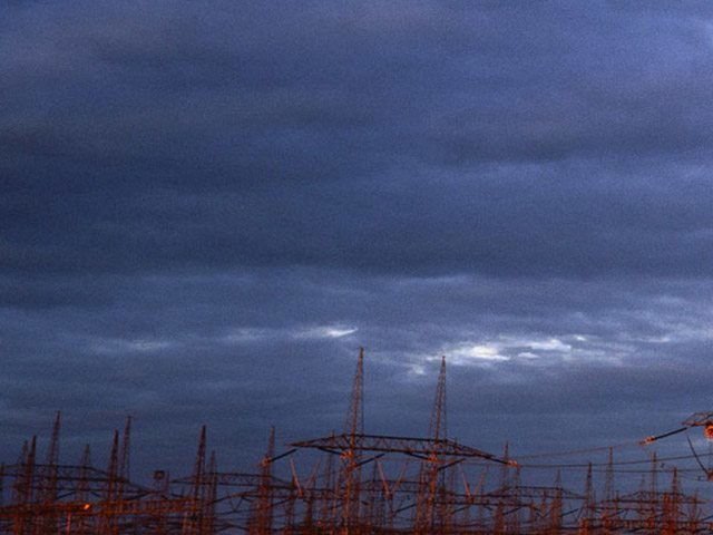 Orange painted transmission tower in front of a dramatic cloudy sky, in the background more transmission towers